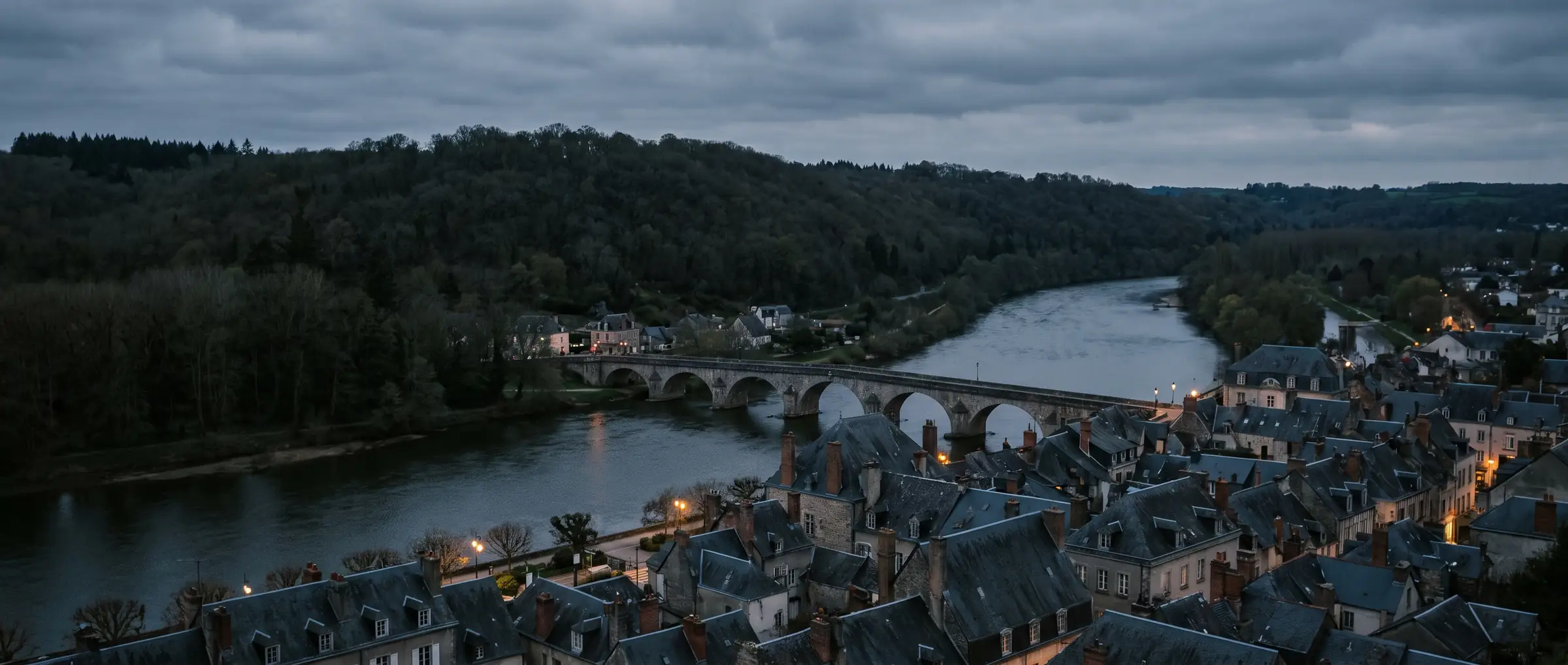 Blick über ein Flusstal mit historischer Altstadt und Brücke in der Dämmerung